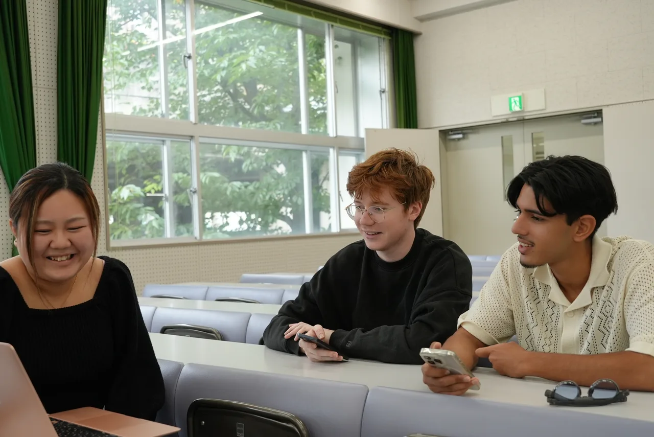 明るい部屋でテーブルを囲み、話し合う3人の学生